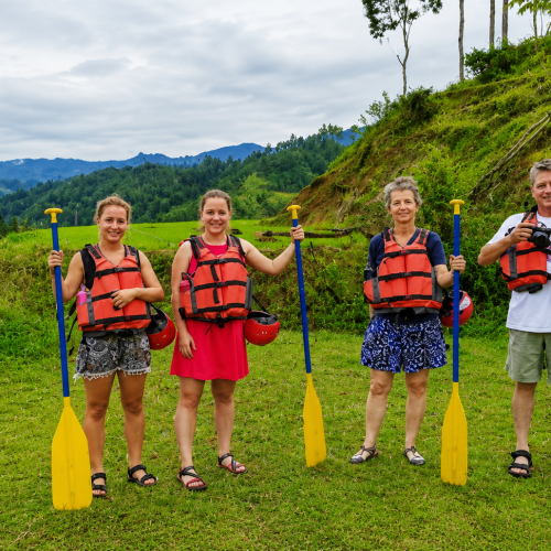 Happy travelers rafting through gentle and exciting rapids in Toraja with panoramic rainforest and mountain views.