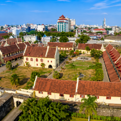 Beautiful view of Fort Rotterdam in Makassar with historic colonial buildings, ancient stone walls, tropical palm trees, and a bright blue sky.